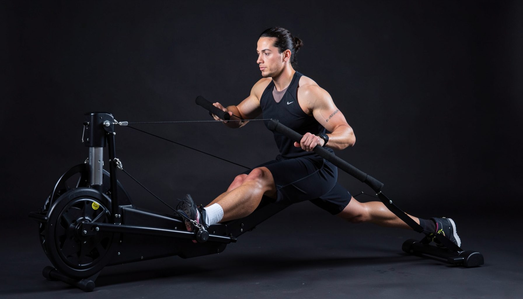A fitness instructor demonstrating rowing technique on an erg machine, focused and professional, dark studio backdrop