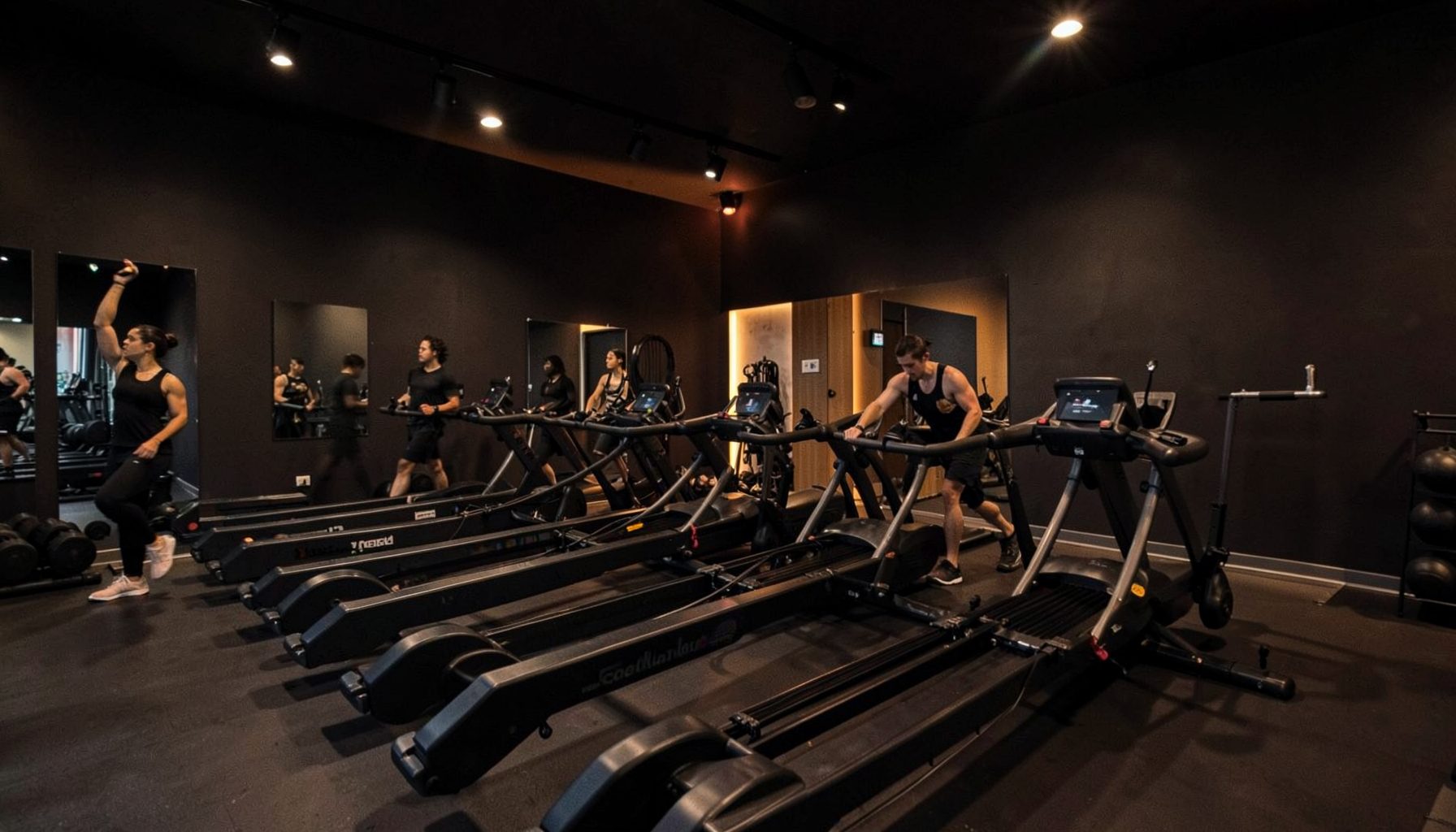 A dimly lit boutique fitness studio with rowing machines lined up, warm amber accent lighting against dark charcoal walls, energetic and modern atmosphere