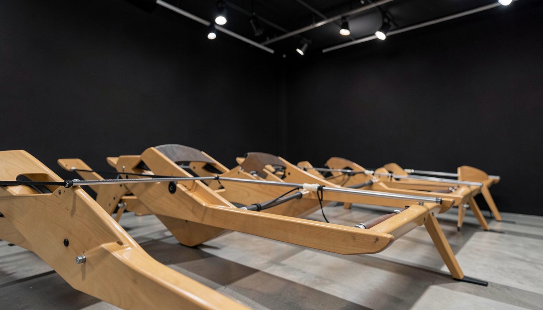 Close-up of sleek wooden water rowing machines in a row inside a modern studio with dark walls and soft overhead track lighting.